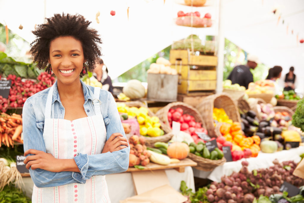 Smiling woman in front of large fruit stand at outdoor market